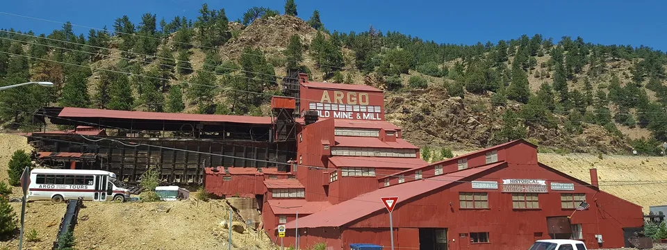 The red Argo gold mill on the hillside above Idaho Springs, its name painted high on the mill, under a blue sky